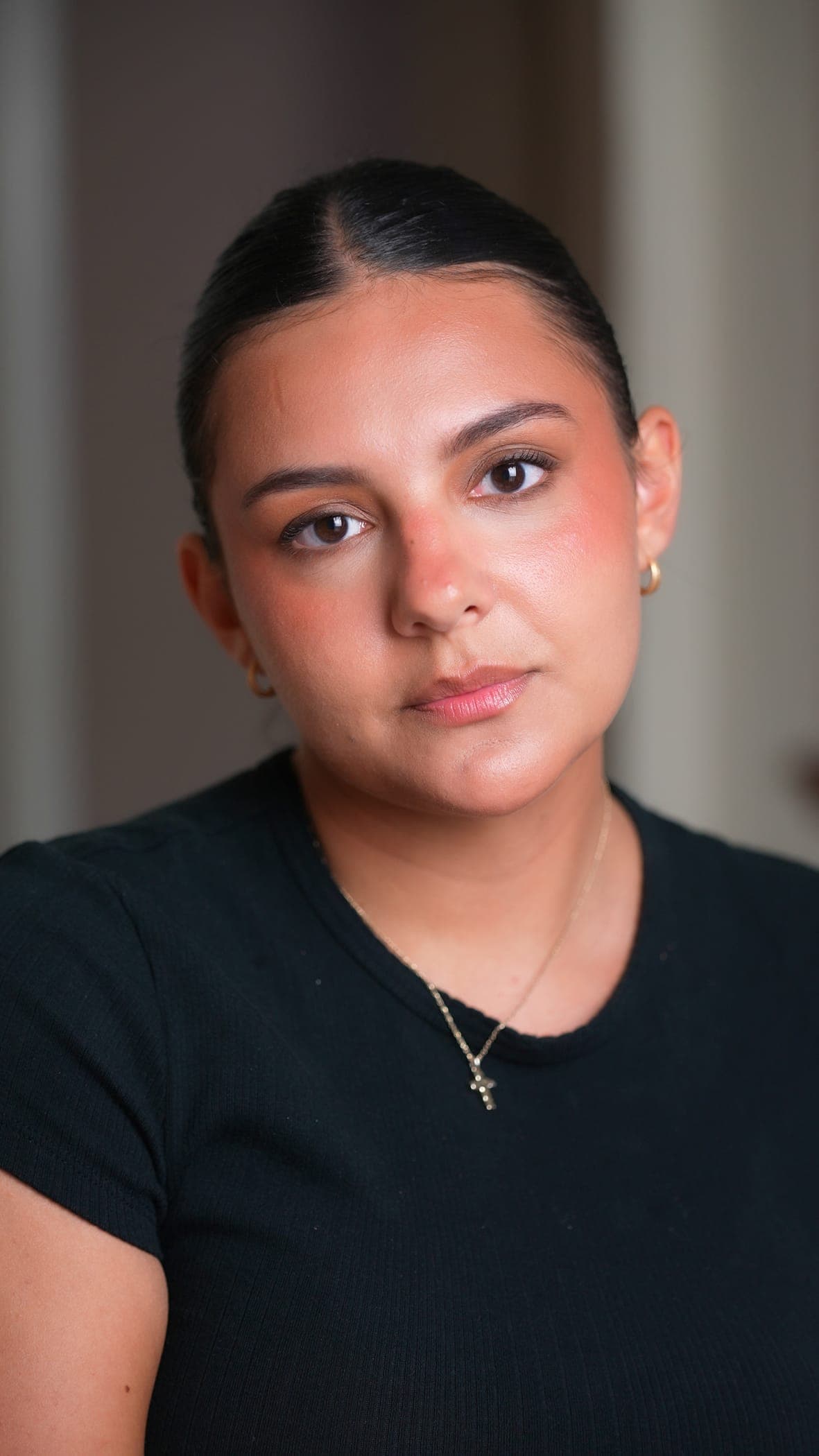 Head-and-shoulders portrait of a client with dark hair pulled back, wearing a soft natural look — defined brows, warm blush, and a neutral lip.
